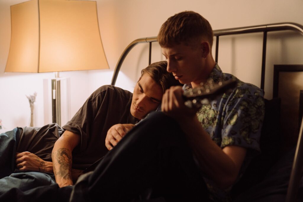 Man in Printed Shirt Playing Guitar Beside Man Leaning on Him