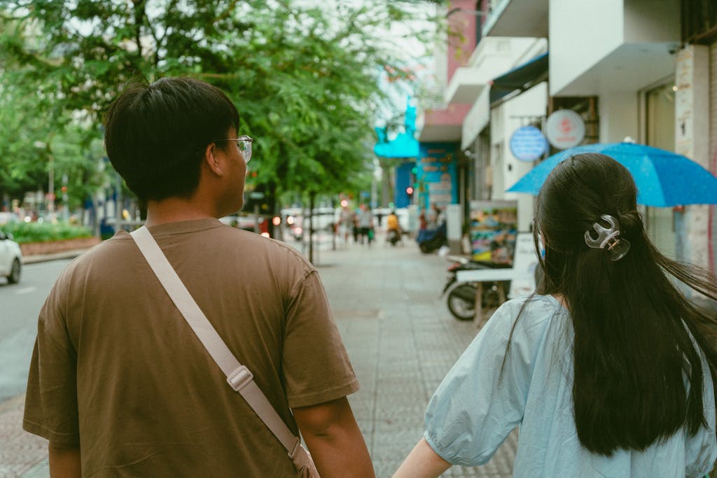 Young couple walking down a vibrant street in Ho Chi Minh City, holding hands under a blue umbrella.